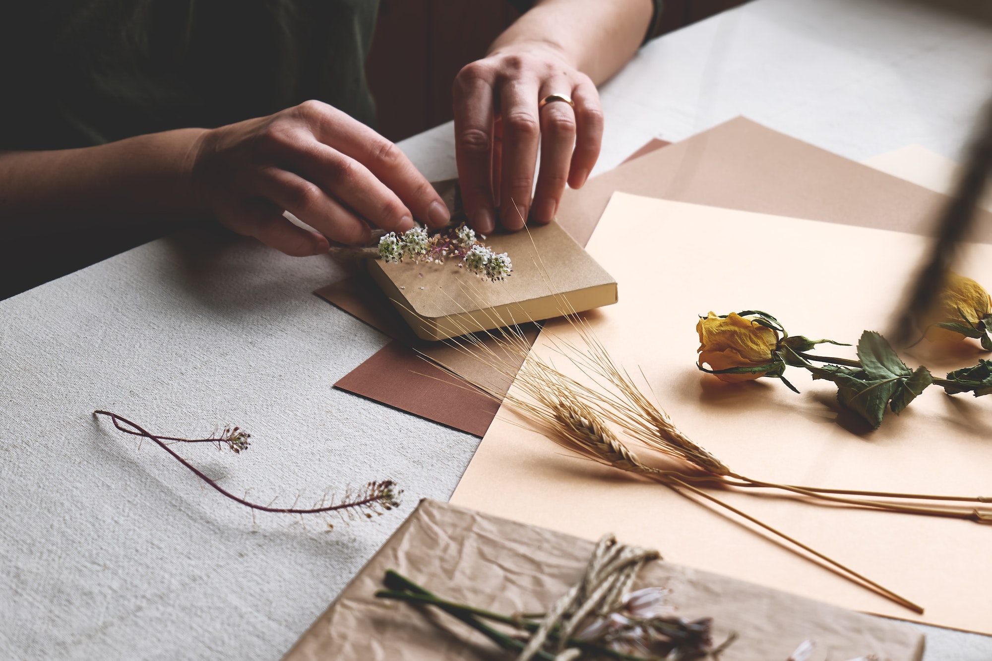 Woman makes trendy hand made gift package with craft recycled paper and dried flowers.